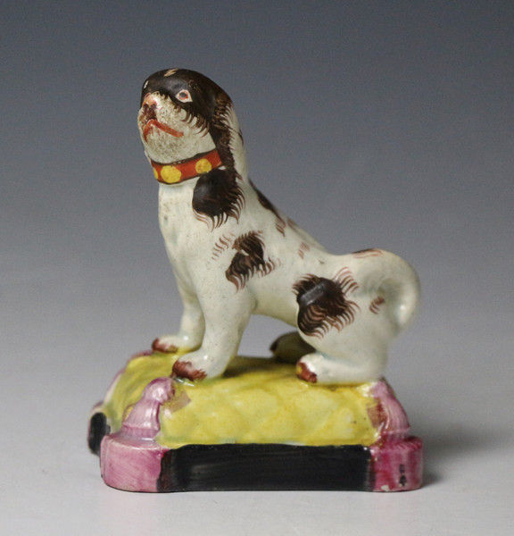 Antique Staffordshire pottery pearlware figure of a dog seated on a cushion base early 19th century England.