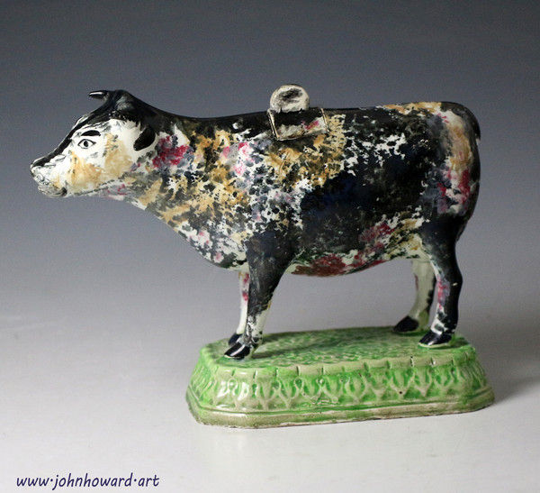 Antique English pottery cow creamer standing on green base early 19th century
