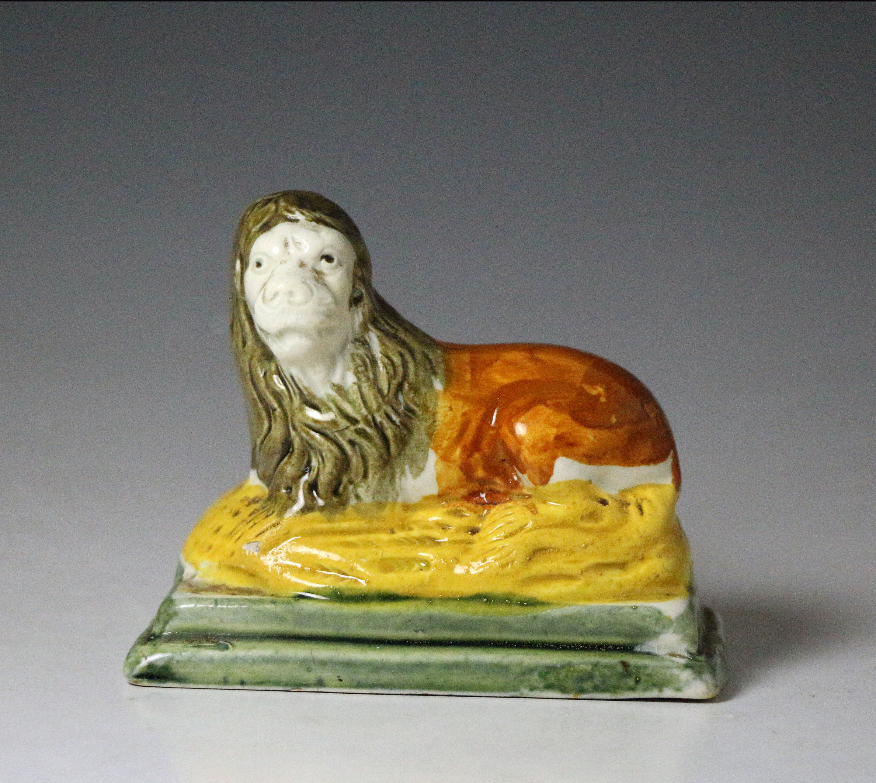Antique English pottery figure of a lion on ochre and green base in Pratt colours , early 19th century