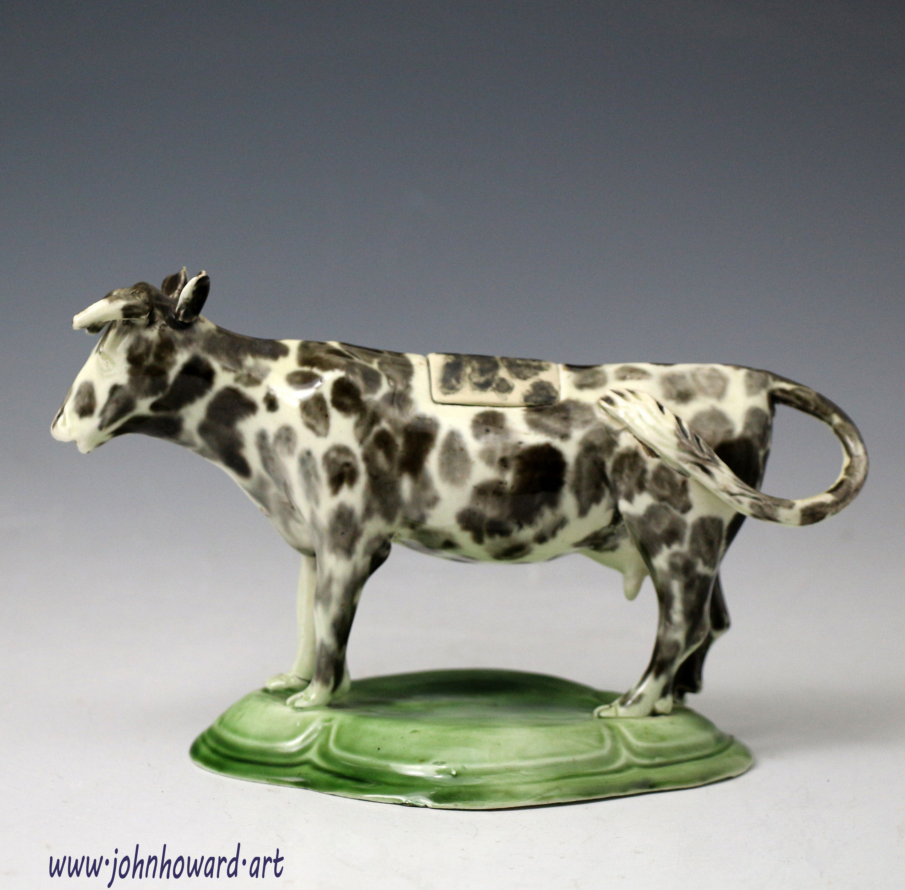 Antique pottery cow creamer figure on green base, a rare early example of small proportions.