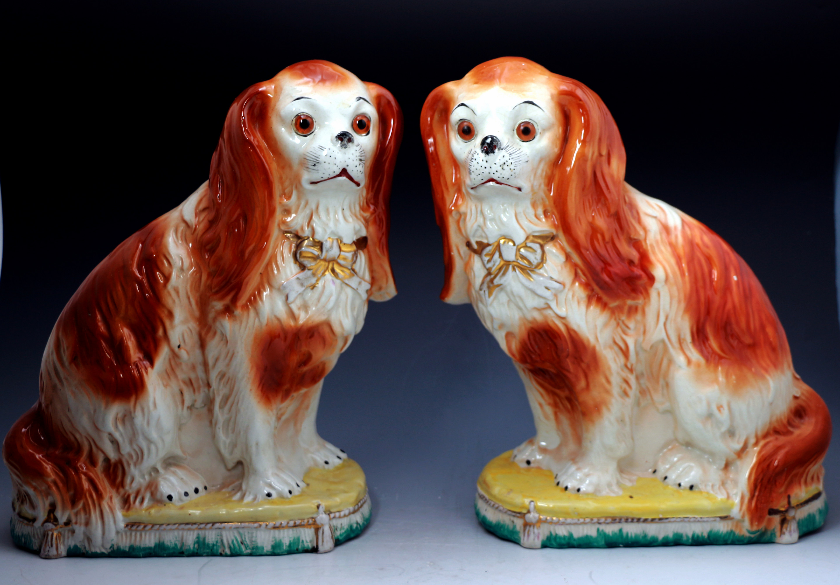 PAIR OF STAFFORDSHIRE POTTERY SPANIELS WITH GLASS EYES SITTING ON CUSHION BASES