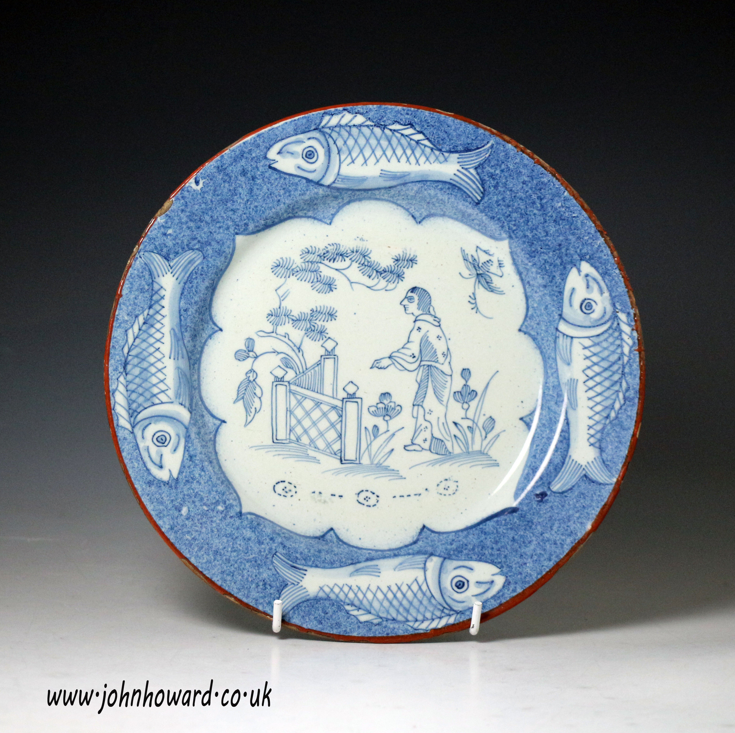 English delftware plate with border decoarted with fish, the centre panel figure in Coriental garden c1740